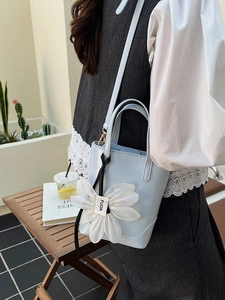 Minimalist light blue bucket bag with white floral charm and adjustable strap