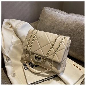 Detail of beige quilted crossbody bag with gold chain strap on white blazer