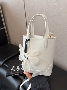 Elegant white bucket handbag with floral charm and gold hardware on black surface