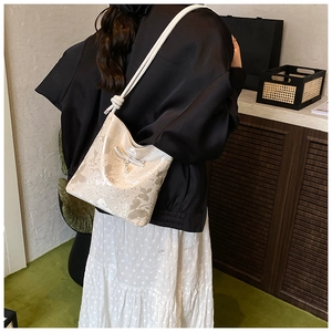 Close-up of a cream bow shoulder bag featuring silver butterfly patterns and a pearl charm
