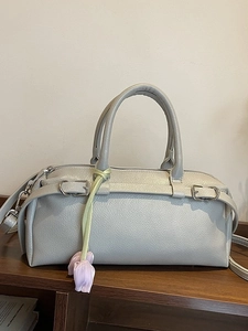 Chic light gray pebbled leather Boston bag with floral charm on a wooden shelf