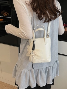White mini bucket bag with flower charm and crossbody strap shown in a lifestyle scene