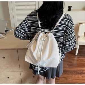 White drawstring bucket backpack shown from back view worn by a model in lifestyle setting