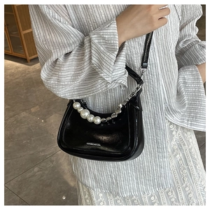 Close-up of black leather croissant bag with gradient pearl chain and metal logo