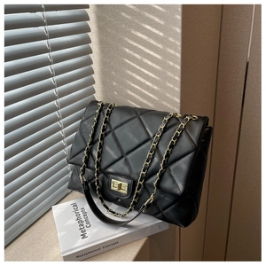Close-up of black quilted leather texture with gold chain strap and metal lock
