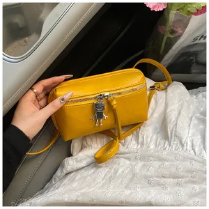 Detail of yellow mini crossbody bag with cute silver robot charm on white dress