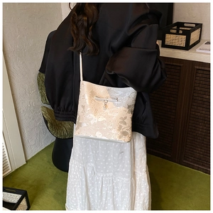 Close-up of beige bow shoulder bag with butterfly patterns and elegant pearl pendant
