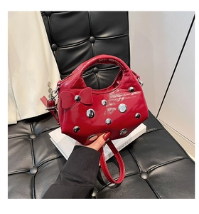 Détail du sac bandoulière en cuir verni rouge avec nœud et rivets métalliques argentés
