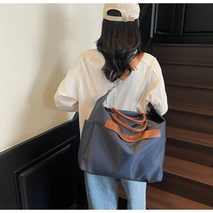 Détail d'un grand sac cabas en nylon bleu avec des anses en cuir marron sur un mannequin