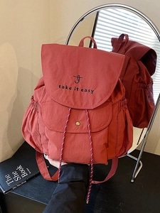 Sac à dos rouge léger en nylon avec broderie élégante présenté devant un miroir de design