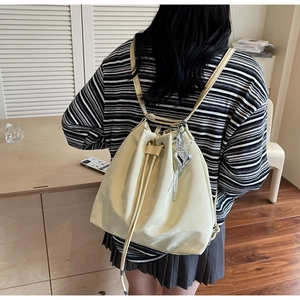 Detail view of cream drawstring bucket backpack with heart charm and tassel detail