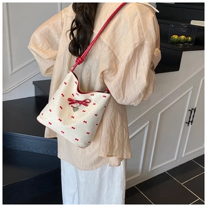 Detail shot of a white bucket bag with red bow prints and a heart-shaped metal pendant