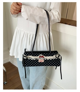 Détail du sac noir à pois avec bordure en dentelle blanche et étiquette à nœud rouge