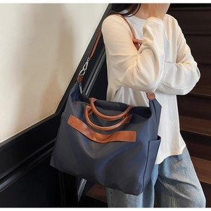 Détail du grand sac cabas en toile bleu marine avec anses en cuir porté par un modèle