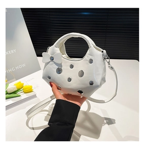 Détail du sac croissant en cuir blanc avec rivets argentés et pendentif noeud