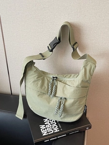 Light green nylon crescent crossbody bag with wide shoulder strap and woven zipper pulls