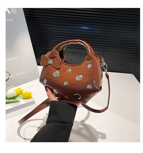 Détail du sac en cuir verni marron avec clous métalliques argentés et nœud décoratif