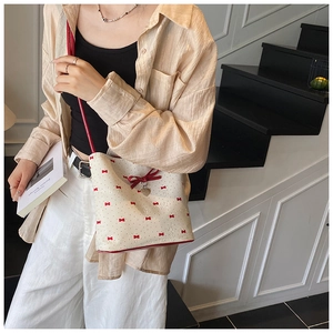 Detail of white bucket bag with red bow print and heart pendant worn by model