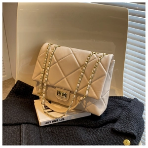Close-up of beige quilted chain bag with gold twist-lock on a modern chair with shadows