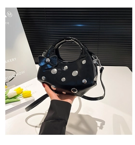 Détail d'un sac à main en cuir verni noir avec clous argentés et nœud bleu scintillant