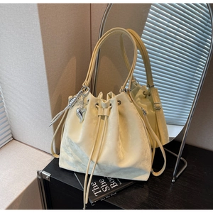 Detail view of a pale yellow bucket bag featuring a silver heart charm and drawstring closure