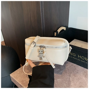 Detail of a creamy white rectangular box bag with a silver robot pendant and slim strap