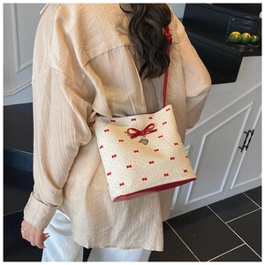 Model wearing a cream shoulder bag with red bow prints and a heart-shaped metal charm