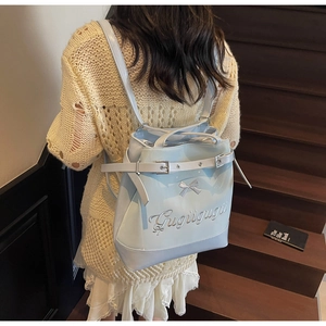 Détail d'un sac à dos bleu clair avec nœud et broderie sur un escalier en bois