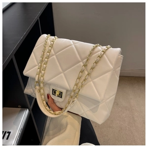 Detail of white quilted handbag showing golden turn-lock clasp and woven chain strap