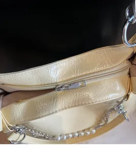 Close-up of smooth metal zipper and pearl chain detail on yellow pleated tote bag