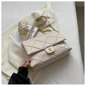 Detailed view of beige quilted leather bag with gold clasp and chain on white blazer