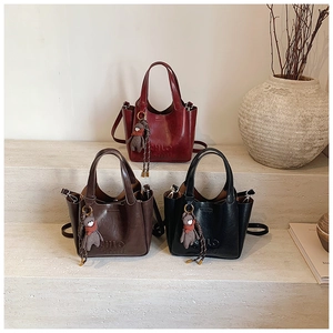 Three minimalist tote bags in burgundy, brown and black with bear charms on stone steps