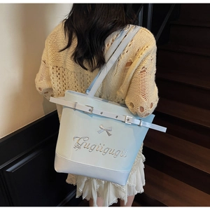 Détail d'un sac cabas bleu clair avec nœud argenté et broderie Gugu sur l'escalier