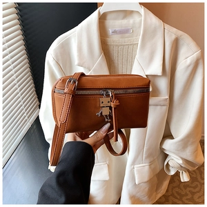 Detail of a brown leather box crossbody bag featuring a unique silver robot metal charm