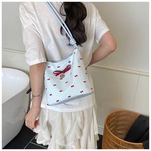 Detail view of light blue bucket bag with red bows, heart charm and drawstring closure