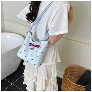 Detail of light blue bow tote bag with red patterns and heart charm on a model's shoulder