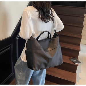 Détail d'un grand sac cabas en nylon noir avec poignées en cuir sur un escalier en bois