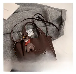 Detail view of dark brown leather handbag with teddy bear charm on grey wool coat