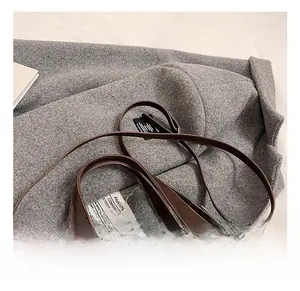 Detail shot of brown leather handbag with gold hardware and long strap on wool fabric