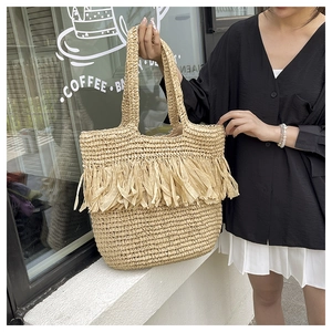 Detail of bohemian woven straw tote bag with tiered fringe accents for beach vacations