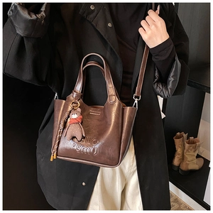 Detail of a dark brown vintage tote bag with a plush bear charm on a black coat model