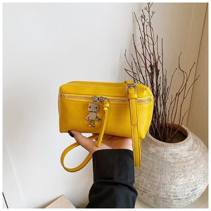 Detail of a bright yellow mini crossbody bag with a robot charm and metal zipper