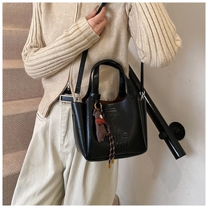 Detail of black synthetic leather tote bag with embossed text and plush bear charm