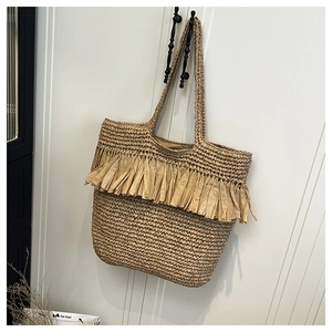 Detail of hand-woven straw tote bag with fringe accents and textured natural fiber surface