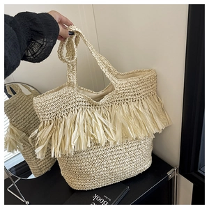 Detail of hand-woven straw tote bag featuring long tassel fringe and bohemian texture