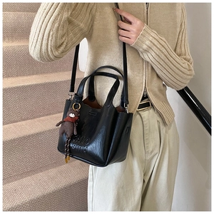 Detail of black leather bucket bag with embossed logo and cute brown bear charm accessory