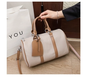 Close-up of cream-colored Boston bag with brown leather trim and pebbled texture