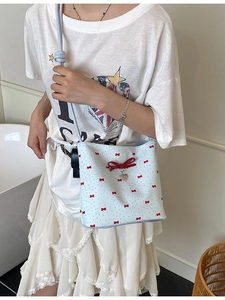 Blue underarm bag with red bow print and heart pendant shown on a model