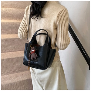 Detail view of black handbag featuring letter embossing and a cute bear charm accessory