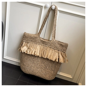Detailed view of handmade straw tote bag with fringe tassels and woven shoulder straps